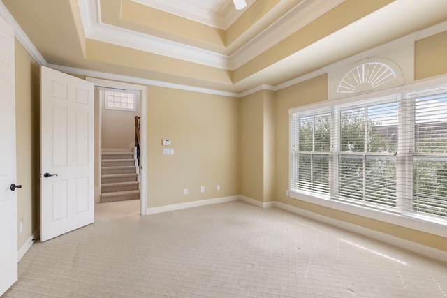 empty room with light carpet, ornamental molding, stairs, a raised ceiling, and a ceiling fan