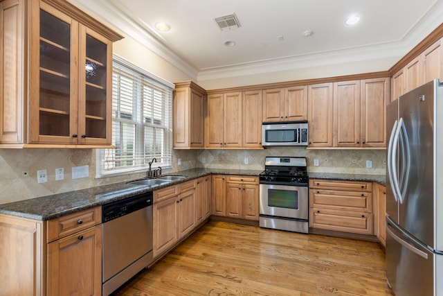 kitchen featuring appliances with stainless steel finishes, a sink, crown molding, glass insert cabinets, and light wood-type flooring