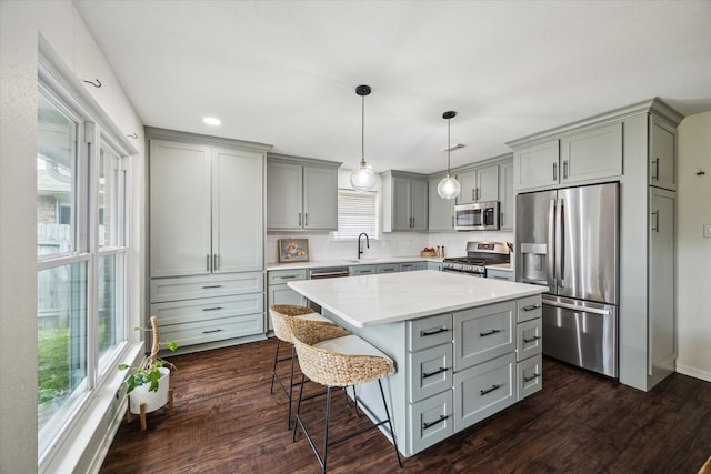 kitchen featuring appliances with stainless steel finishes, gray cabinets, a sink, dark wood-style flooring, and a breakfast bar