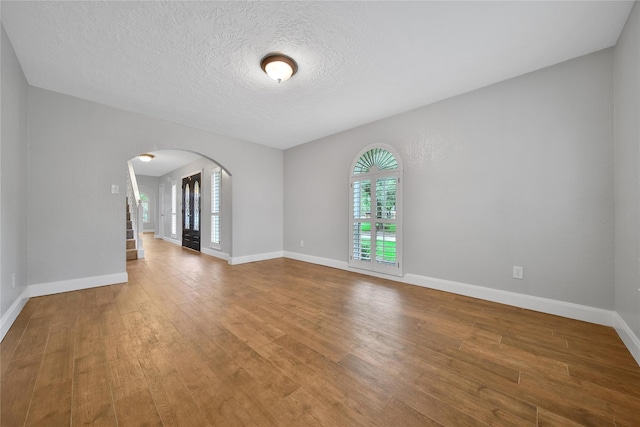 12443 Honeywood Trl, Houston, TX 77077 - spare room featuring arched walkways, wood finished floors, baseboards, a textured ceiling, and stairway