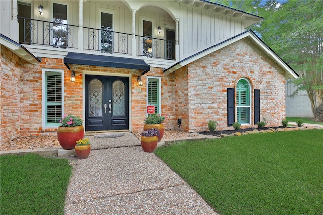 12443 Honeywood Trl, Houston, TX 77077 - view of exterior entry with a balcony, board and batten siding, french doors, brick siding, and a lawn