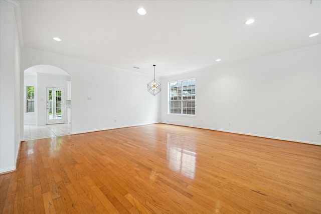 spare room featuring arched walkways, light wood-type flooring, recessed lighting, baseboards, and ornamental molding
