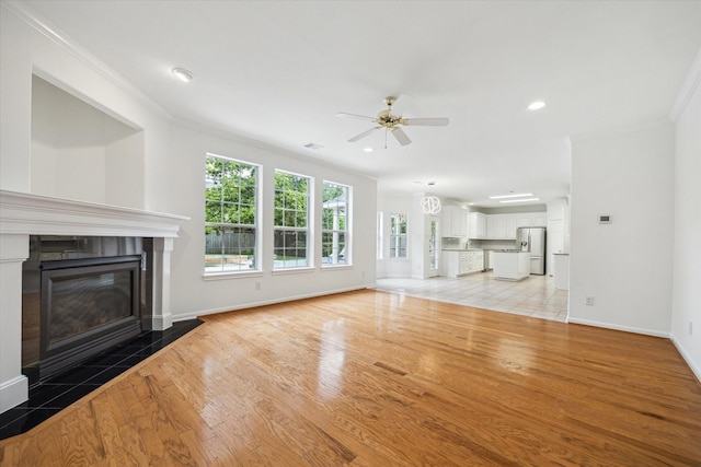 unfurnished living room with crown molding, light wood-style flooring, baseboards, ceiling fan, and a tiled fireplace