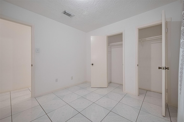 unfurnished bedroom featuring light tile patterned floors, a textured ceiling, two closets, and baseboards