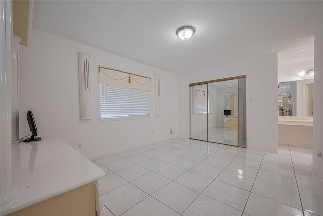 unfurnished bedroom with a textured ceiling, light tile patterned flooring, a closet, and multiple windows
