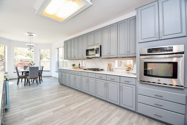20011 Polly Creek Way, Katy, TX 77450 - kitchen with gray cabinets, stainless steel appliances, light wood finished floors, light countertops, and decorative light fixtures