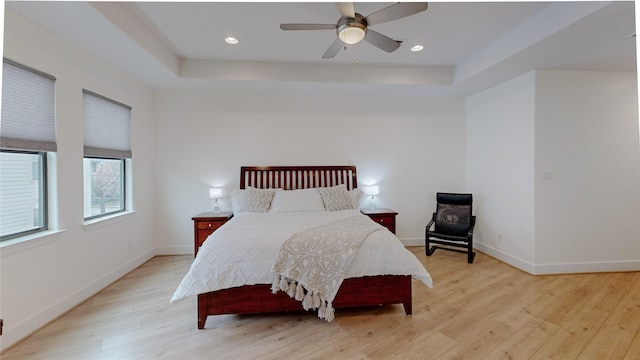 bedroom with light wood-style floors, a raised ceiling, baseboards, ceiling fan, and recessed lighting