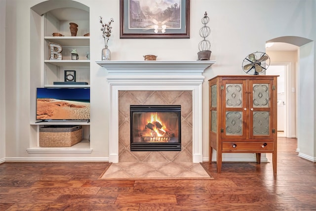 detailed view of wood finished floors, arched walkways, built in features, a premium fireplace, and baseboards