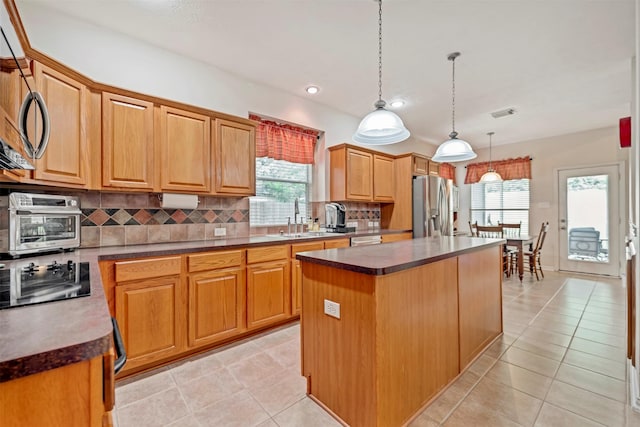 kitchen with appliances with stainless steel finishes, a sink, backsplash, a center island, and light tile patterned floors