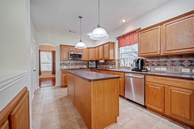 kitchen featuring appliances with stainless steel finishes, a sink, arched walkways, dark countertops, and recessed lighting