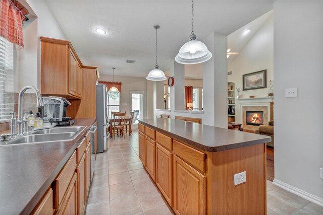 kitchen with a sink, dark countertops, a kitchen island, a warm lit fireplace, and recessed lighting