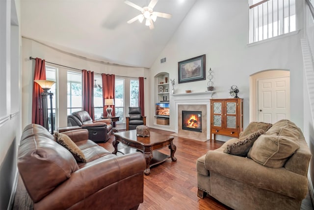 living room with high vaulted ceiling, built in shelves, a ceiling fan, a fireplace, and wood finished floors