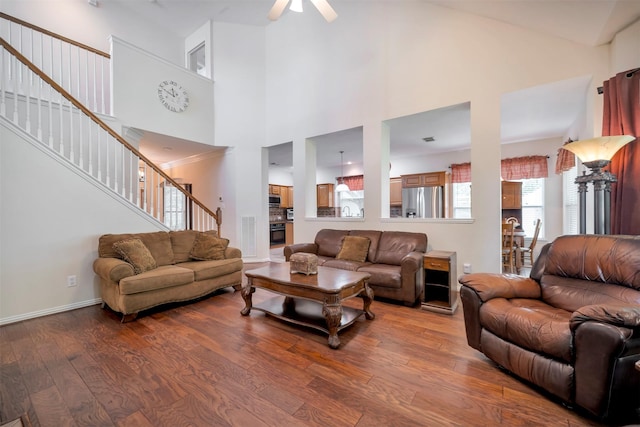 living area with wood finished floors, stairway, ceiling fan, and a towering ceiling
