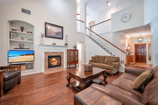 living area with a high ceiling, wood finished floors, built in shelves, stairway, and a high end fireplace