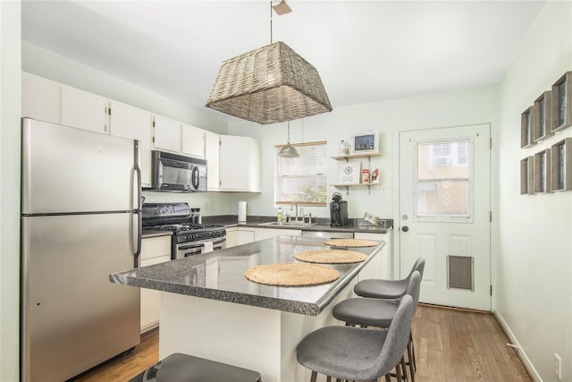 1614 Ursuline St, Galveston, TX 77550 - kitchen featuring stainless steel appliances, a sink, dark countertops, white cabinetry, and wood finished floors
