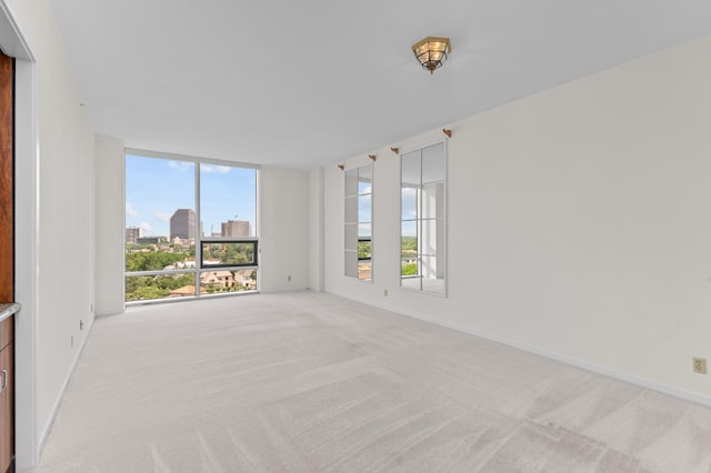 unfurnished room with light carpet, plenty of natural light, floor to ceiling windows, baseboards, and a view of city