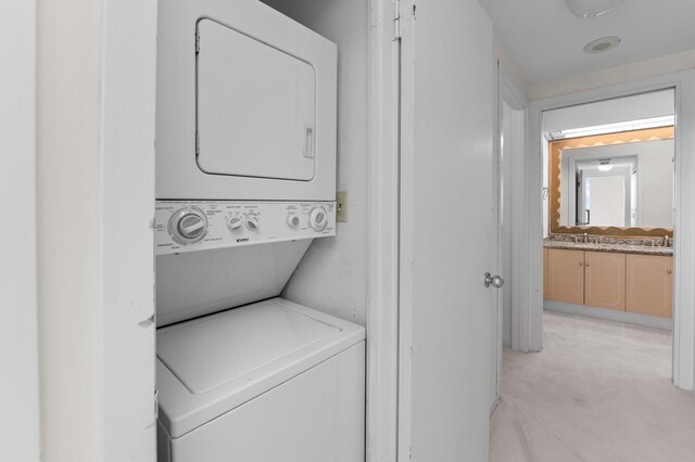 clothes washing area with stacked washer and clothes dryer and light colored carpet