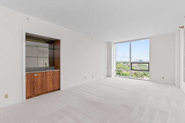 unfurnished living room with light colored carpet, bar with sink, and expansive windows