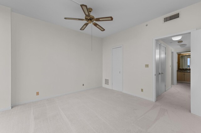 empty room featuring light colored carpet, a ceiling fan, and baseboards