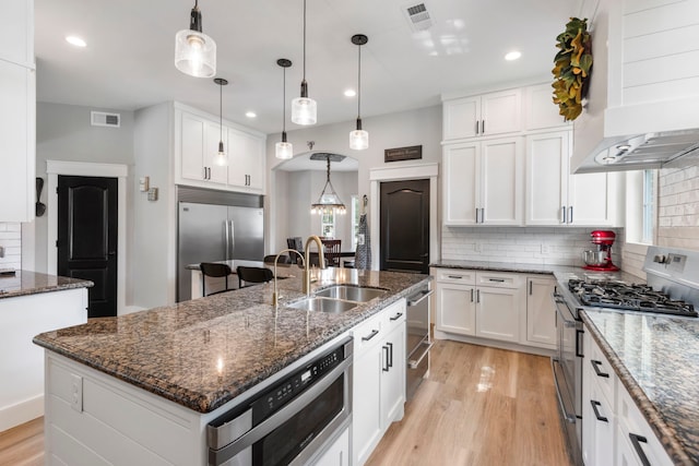 4810 Pine Wood Meadows Ln, Spring, TX 77386 - kitchen featuring appliances with stainless steel finishes, wall chimney exhaust hood, a sink, light wood finished floors, and backsplash