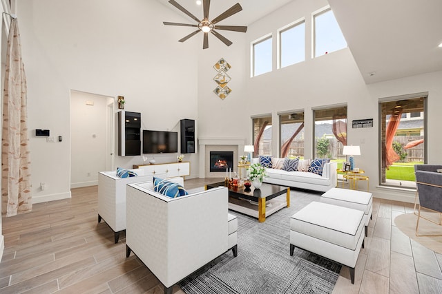 28946 Parker Ridge Dr, Katy, TX 77494 - living room featuring ceiling fan, a towering ceiling, light wood-style floors, baseboards, and a glass covered fireplace
