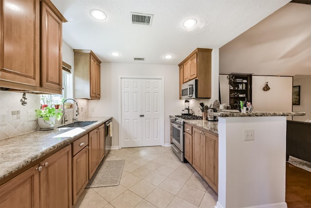 12938 Dermott Dr, Houston, TX 77065 - kitchen featuring stainless steel appliances, a sink, light stone countertops, a peninsula, and brown cabinets