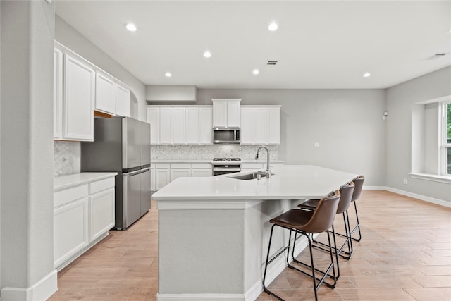 2411 Jitterbug Ln, Katy, TX 77493 - kitchen with a sink, appliances with stainless steel finishes, decorative backsplash, a kitchen island with sink, and light wood-style floors