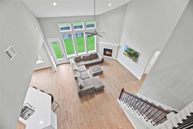 2411 Jitterbug Ln, Katy, TX 77493 - living room featuring a high ceiling, ceiling fan, a warm lit fireplace, light wood-type flooring, and baseboards