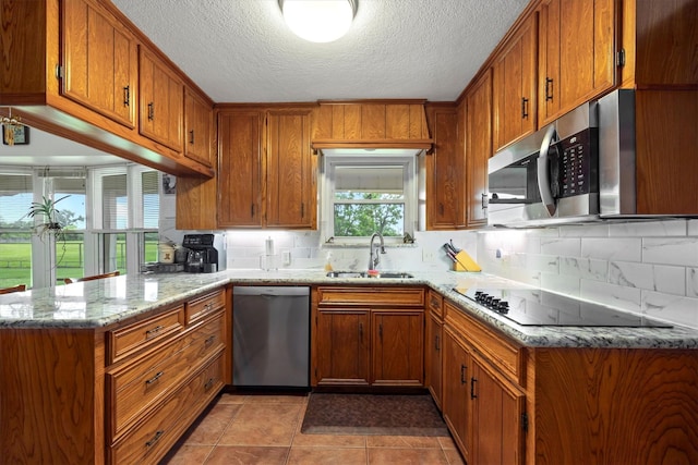 6825 Highland Rd, Santa Fe, TX 77517 - kitchen featuring appliances with stainless steel finishes, a sink, brown cabinetry, a peninsula, and backsplash
