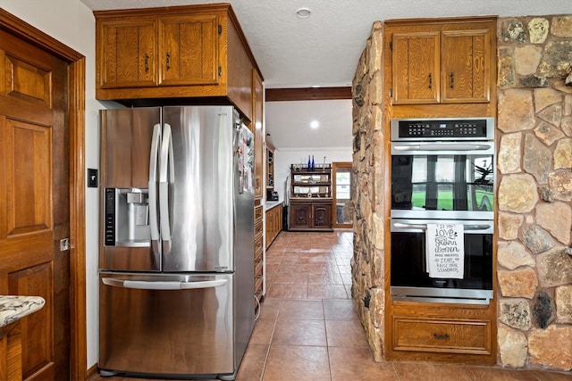 6825 Highland Rd, Santa Fe, TX 77517 - kitchen with appliances with stainless steel finishes, brown cabinetry, tile patterned flooring, and a textured ceiling