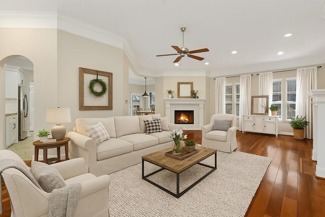 living area featuring arched walkways, a ceiling fan, plenty of natural light, ornamental molding, and a lit fireplace