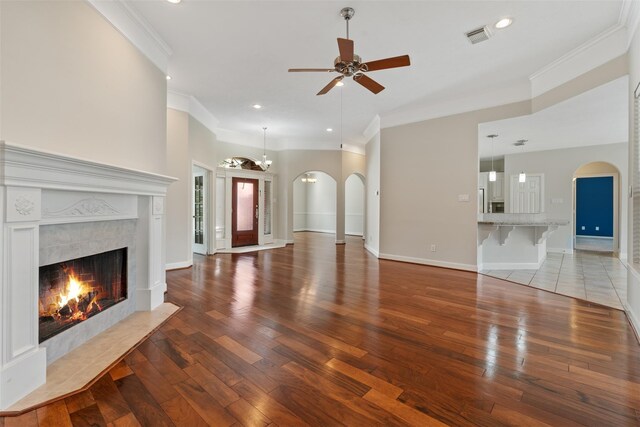 unfurnished living room featuring a fireplace, arched walkways, hardwood / wood-style flooring, crown molding, and a ceiling fan