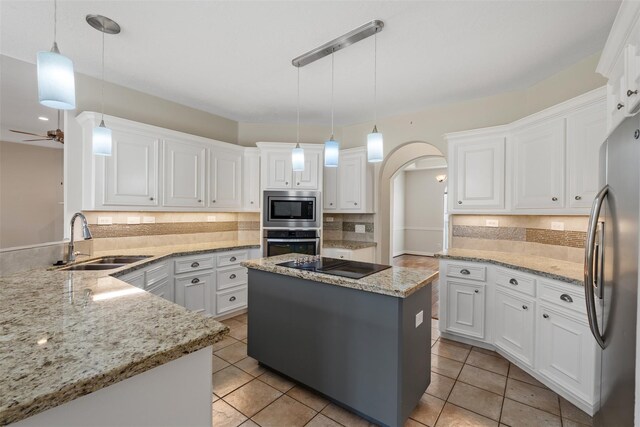 kitchen featuring appliances with stainless steel finishes, a sink, arched walkways, decorative backsplash, and a ceiling fan