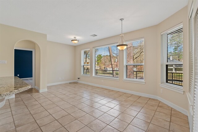 unfurnished dining area with light tile patterned floors, baseboards, and arched walkways