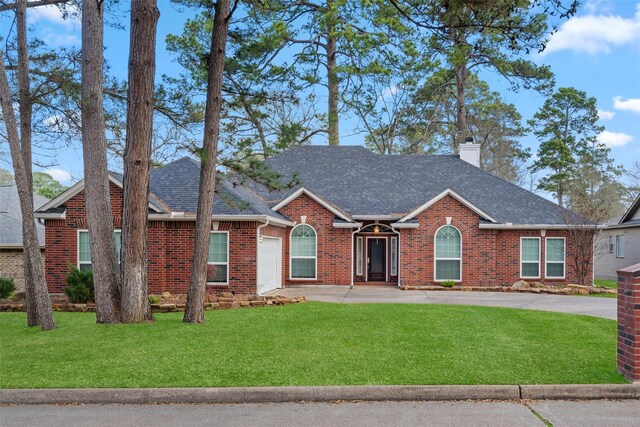 view of front of home with an attached garage, a chimney, brick siding, driveway, and a front yard