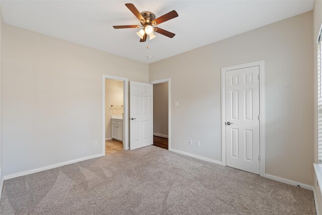 unfurnished bedroom featuring light carpet, baseboards, connected bathroom, and a ceiling fan