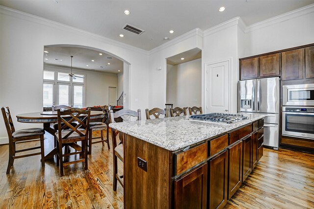 kitchen featuring stainless steel appliances, a kitchen breakfast bar, wood finished floors, arched walkways, and crown molding