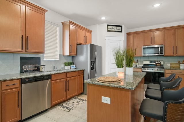 kitchen with stainless steel appliances, a breakfast bar area, decorative backsplash, a center island, and light stone counters