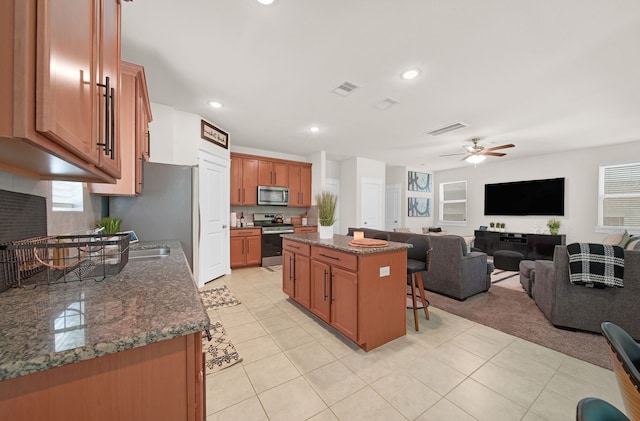 kitchen with stainless steel appliances, a kitchen island, ceiling fan, a kitchen bar, and open floor plan