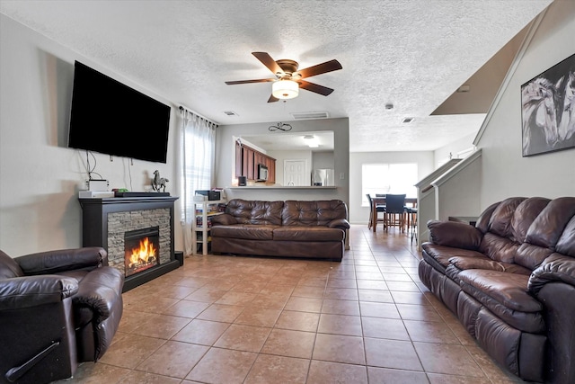 tiled living area featuring a textured ceiling, ceiling fan, and a stone fireplace