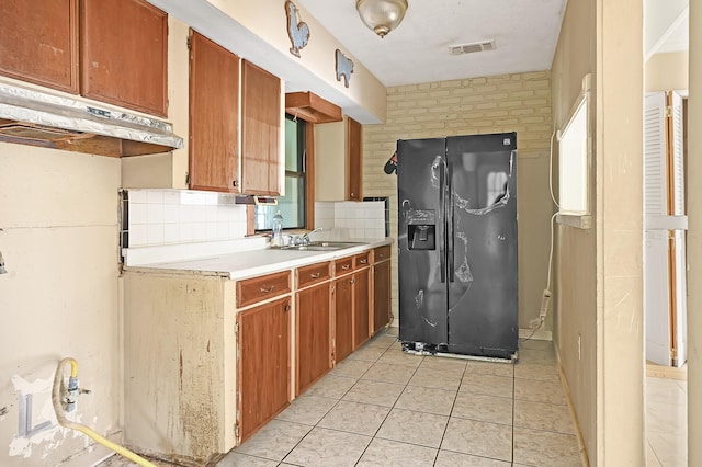 kitchen featuring black refrigerator with ice dispenser, a sink, light countertops, under cabinet range hood, and light tile patterned floors