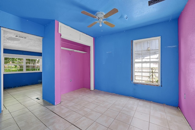 unfurnished bedroom featuring a textured ceiling, tile patterned floors, a closet, and a ceiling fan