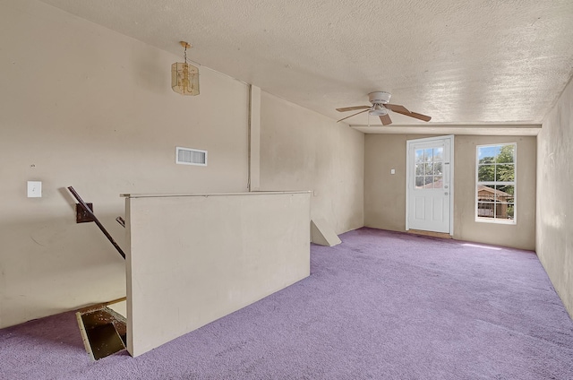 unfurnished living room featuring carpet, a ceiling fan, and a textured ceiling