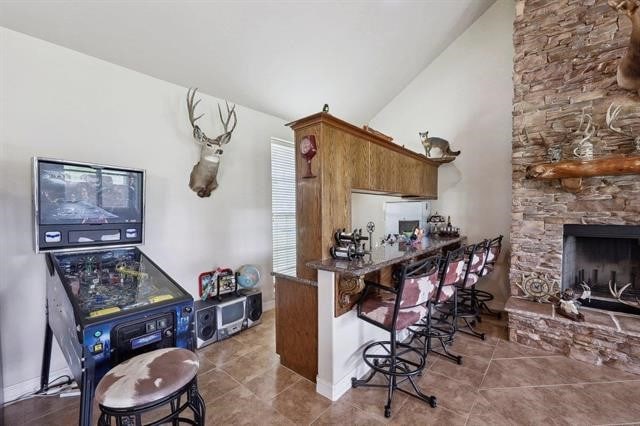 2014 Fish Lake Rd, Kountze, TX 77625 - kitchen with brown cabinets, vaulted ceiling, a stone fireplace, tile patterned floors, and a kitchen breakfast bar