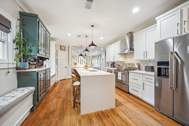 kitchen with stainless steel appliances, wall chimney exhaust hood, a sink, light countertops, and recessed lighting