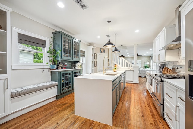 kitchen with range with two ovens, a sink, glass insert cabinets, a kitchen island with sink, and tasteful backsplash