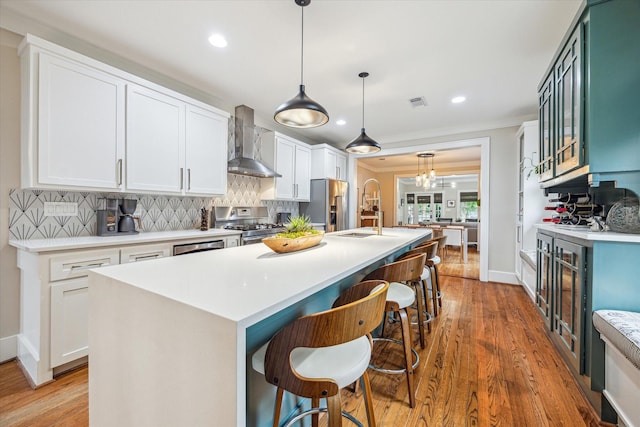 813 Key St, Houston, TX 77009 - kitchen featuring wall chimney range hood, stainless steel appliances, tasteful backsplash, an island with sink, and light wood-type flooring