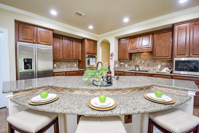 7003 Paxton Ct, Sugar Land, TX 77479 - kitchen featuring stainless steel appliances, arched walkways, tasteful backsplash, light stone counters, and a large island