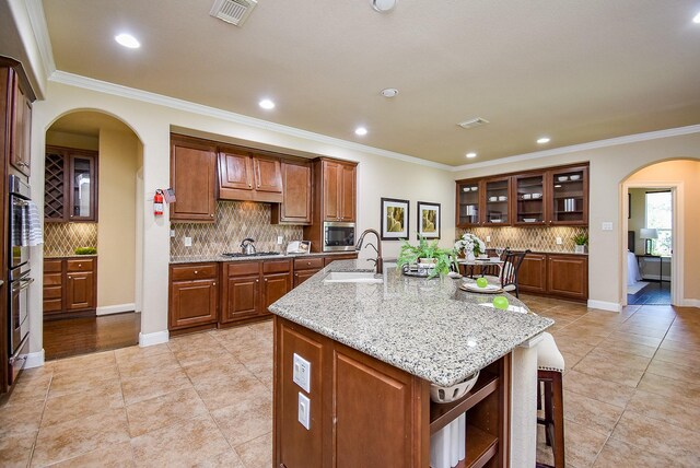 7003 Paxton Ct, Sugar Land, TX 77479 - kitchen featuring arched walkways, a sink, decorative backsplash, a center island with sink, and stainless steel appliances