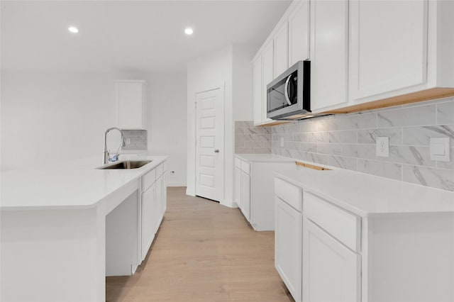 kitchen with a sink, stainless steel microwave, light wood-type flooring, decorative backsplash, and recessed lighting